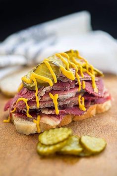 a sandwich with pickles and mustard drizzled over it on a cutting board