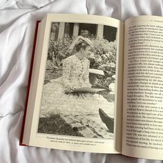 an open book with a woman sitting on a bed in front of flowers and plants