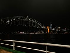 the sydney bridge is lit up at night as seen from across the water on a boat