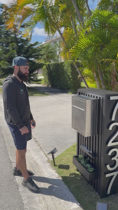 a man standing next to a trash can on the side of a road with palm trees in the background