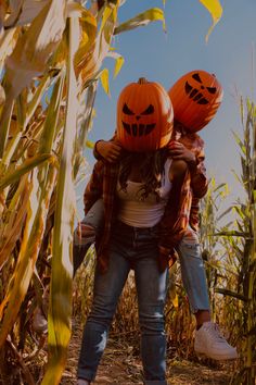 two people wearing pumpkin heads in a cornfield with blue sky behind them and one person holding the head of another