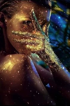 a woman's face is covered in gold glitter and has her hands to her face