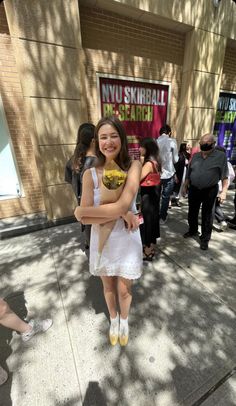 a girl in white dress holding a bouquet of flowers and smiling at the camera with people walking by