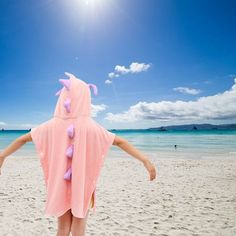 a girl in a pink poncho on the beach with her arms spread out