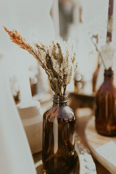 some dried flowers are in a brown glass vase on a table next to other bottles