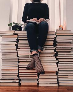 a woman sitting on top of a stack of books with her legs crossed and reading