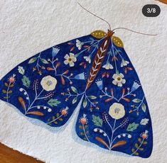 a painting of a blue butterfly with flowers on it's wings, sitting on top of a piece of paper