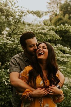 a man and woman standing next to each other in front of some trees with white flowers