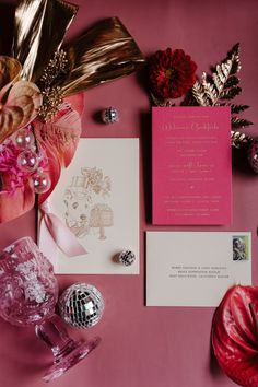 the wedding stationery is laid out on top of pink paper and silver decorations, including an ornament