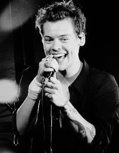 a young man singing into a microphone in front of a black and white photo with lights behind him