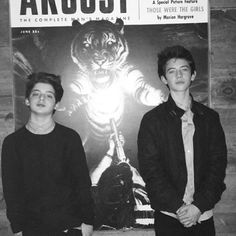 two people standing next to each other in front of an advertisement for argosy