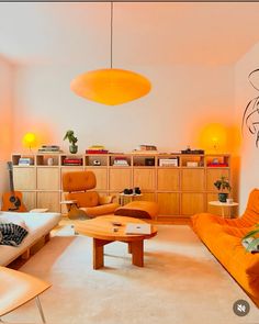 a living room filled with lots of furniture and orange lights hanging from the ceiling above