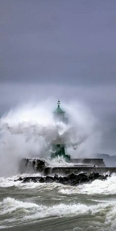 the lighthouse is surrounded by large waves in the ocean and it looks like it's crashing