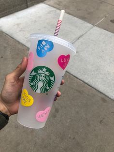 a hand holding a starbucks cup with hearts and stickers on the side of it