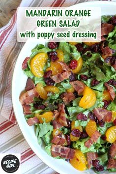 a salad with oranges, bacon and cranberries in a white bowl on a striped cloth