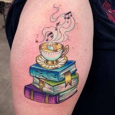 a woman with a tattoo on her arm is holding a stack of books and a cup of coffee