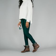 a woman in green pants and boots is posing for the camera with her hand on her hip