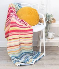 a white chair with a yellow pillow on it and a multicolored knitted blanket