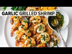 grilled shrimp with garlic and parsley on a white plate next to a small bowl of dipping sauce