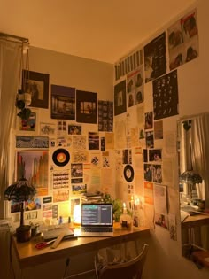 a laptop computer sitting on top of a wooden desk in front of a wall covered with pictures