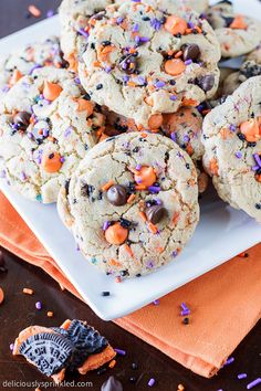 cookies with sprinkles and chocolate chips on a white plate next to an orange napkin