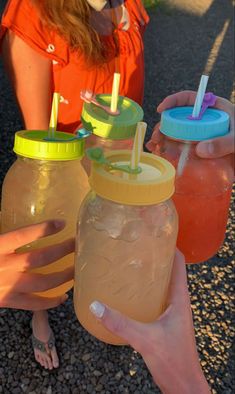 three people holding mason jars with straws and drinks in them on the ground outside