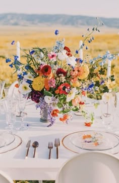 the table is set with flowers, candles and wine glasses for an outdoor dinner party