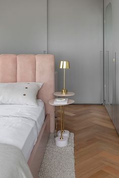 a white bed sitting next to a pink headboard on top of a wooden floor