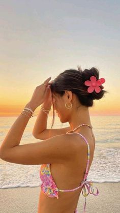 a woman standing on top of a beach next to the ocean wearing a pink flower in her hair