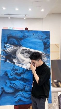 a man standing in front of a blue painting on a easel while talking on his cell phone