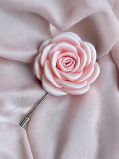 a pink rose on top of a satin fabric with a metal pin in the middle