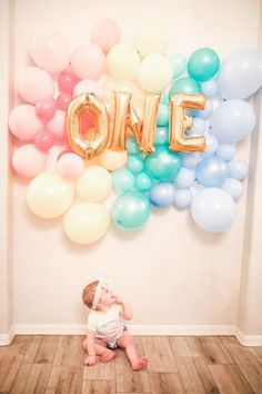 a baby sitting on the floor in front of balloons that spell out'one '