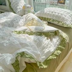 a bed with white and green ruffled bedspread, pillows and a teddy bear