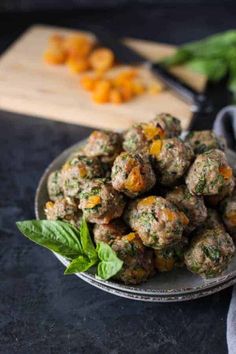 a plate filled with meatballs and garnished with green leaves next to a cutting board