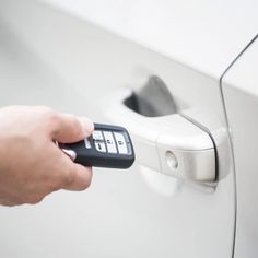 a hand is holding a remote control to a car door handle and pressing the button