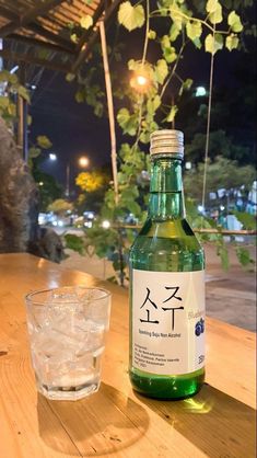 a bottle of water sitting on top of a wooden table next to a glass filled with ice