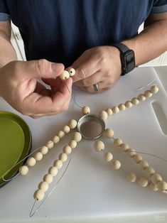 a man is making bead necklaces out of beads on a white table top