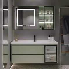 a bathroom with grey walls and white counter tops, lighted mirrors above the vanity area