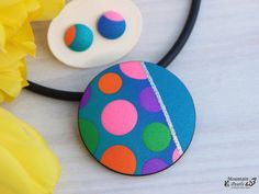 a necklace with colorful polka dots on it next to yellow flowers and a flower pot