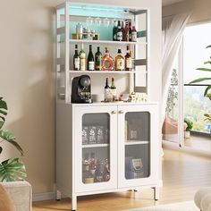 a white cabinet filled with lots of bottles and liquor on it's shelves next to a potted plant