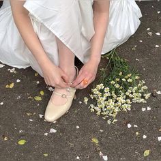 a woman in white dress tying shoes next to flowers