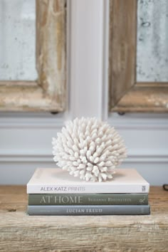 a stack of three books sitting on top of a wooden table next to two windows