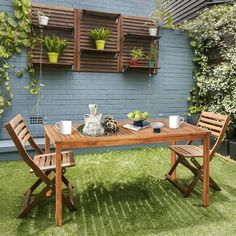 a wooden table sitting on top of a lush green field next to a blue wall