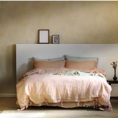 a bed with pink linens and pillows in a neutral colored bedroom, along with two framed pictures on the wall