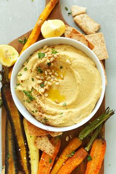 a bowl of hummus and carrots on a cutting board with crackers next to it