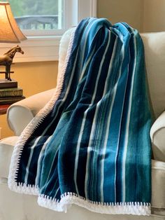 a blue and white striped blanket sitting on top of a couch next to a lamp