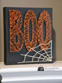 the word boo spelled out in orange string on a black canvas mounted to a fireplace mantel