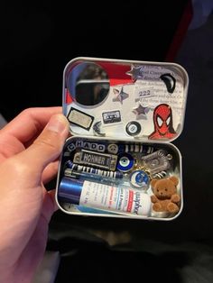 someone is holding an open tin with various items in it, including a teddy bear