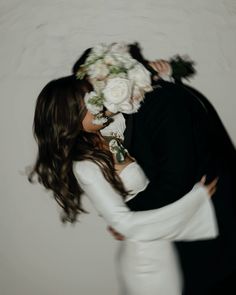 a bride and groom kissing in front of a white wall with flowers on their head