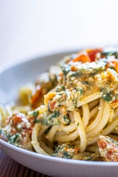 a white bowl filled with pasta and sauce on top of a wooden table next to a fork